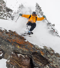 Person skiing down a snowy slope with trees and rocks in the background